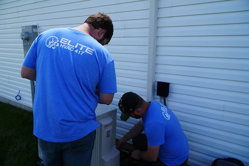 2 blue worker Elite HVAC 417 technicians installing and servicing an outdoor heat pump system.